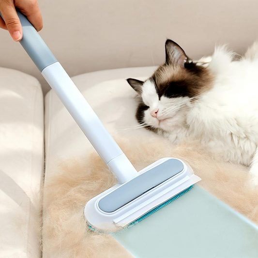 Person using a cleaning tool on a couch with a cat sitting nearby